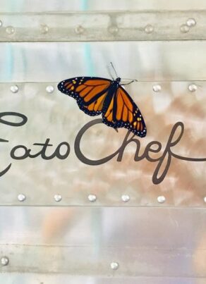 A monarch butterfly rests on a metallic sign that reads EatoChef in cursive script, attached to a riveted metal surface.