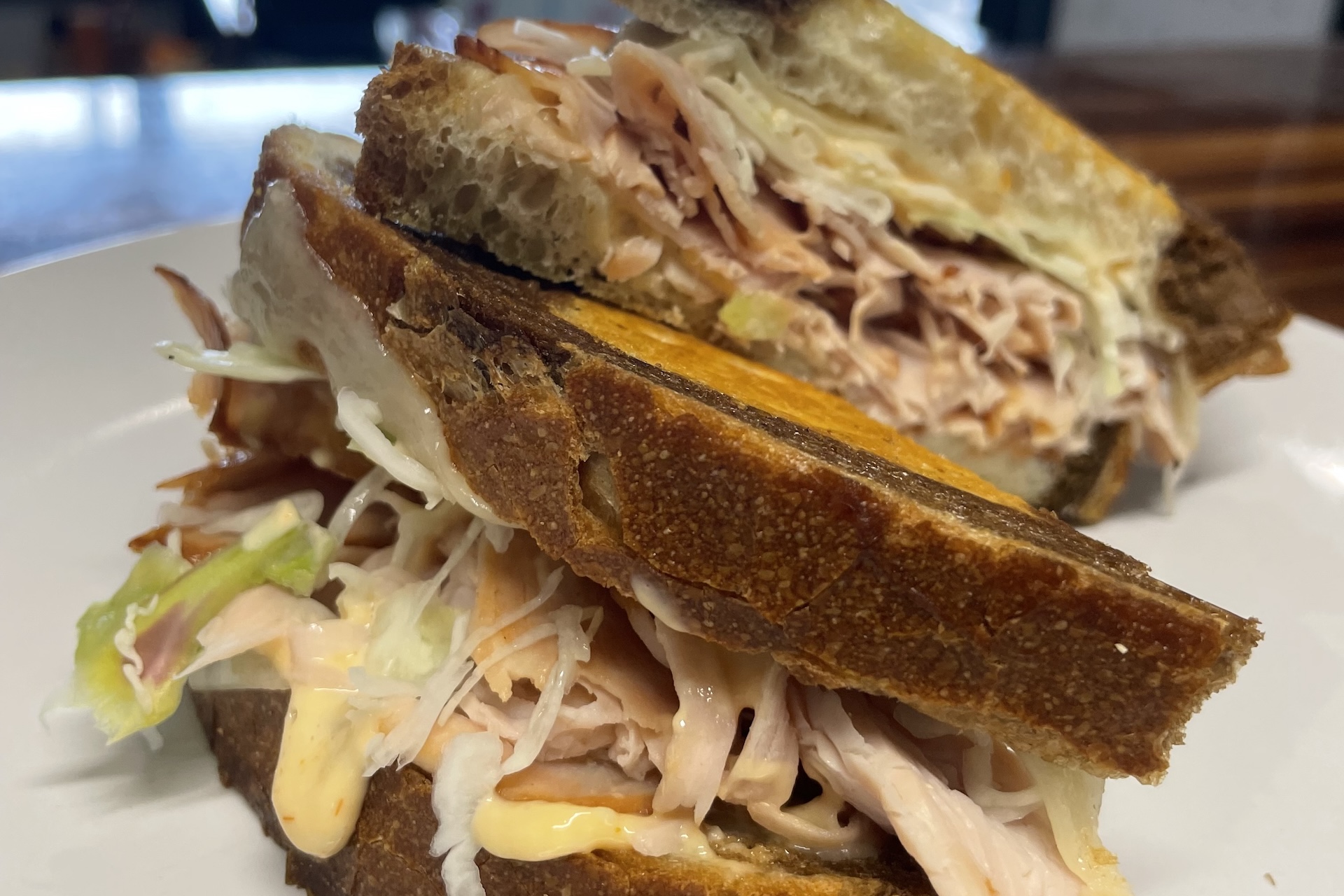 Two thick slices of toasted bread filled with shredded turkey, lettuce, and a creamy sauce, stacked on a white plate.