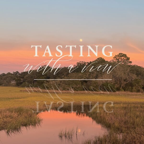 A sunset sky in shades of pink and orange reflects on a calm marsh with tall grasses; text over the image reads, Tasting with a view.