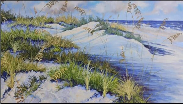 A beach scene with white sand dunes covered in green grass and sea oats, set against a blue sky and ocean in the background.
